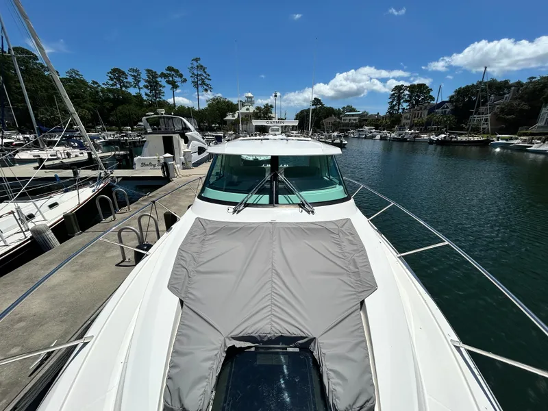 Slide: The Image of 2023 Tiara Yachts 43 LE docked in a scenic marina under a clear blue sky. - 4