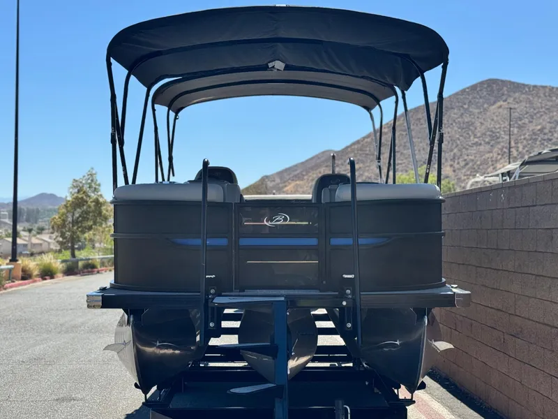 Slide: The Image of 2023 Barletta Cabrio 24UC pontoon boat with canopy, parked on a trailer, mountain backdrop. - 2