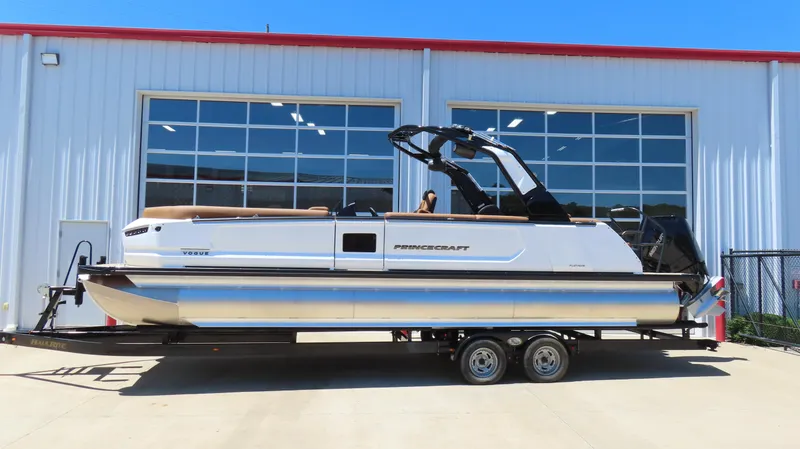 The Image of 2025 Princecraft Vogue 27 RL pontoon boat on trailer, parked outside a building. - 0