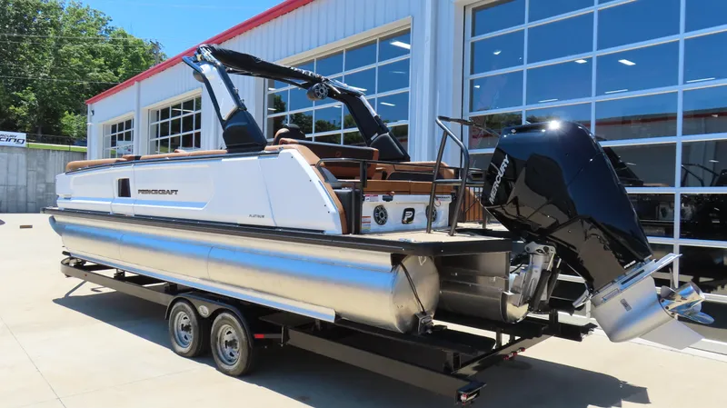 Slide: The Image of 2025 Princecraft Vogue 27 RL pontoon boat on trailer, parked outside a modern building. - 4