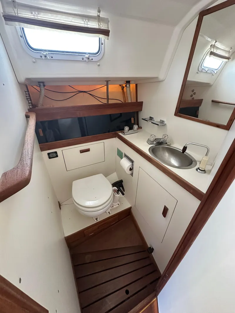 Slide: The Image of 1986 Sabre 32 yacht bathroom with toilet, sink, mirror, and wooden accents. - 13