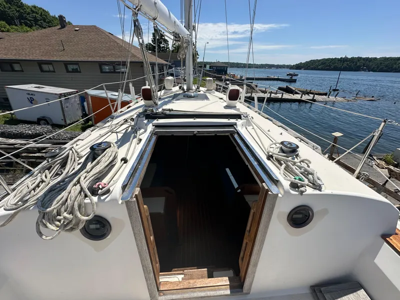 Slide: The Image of 1986 Sabre 32 sailboat deck view with open cabin, docked by a scenic waterfront. - 6