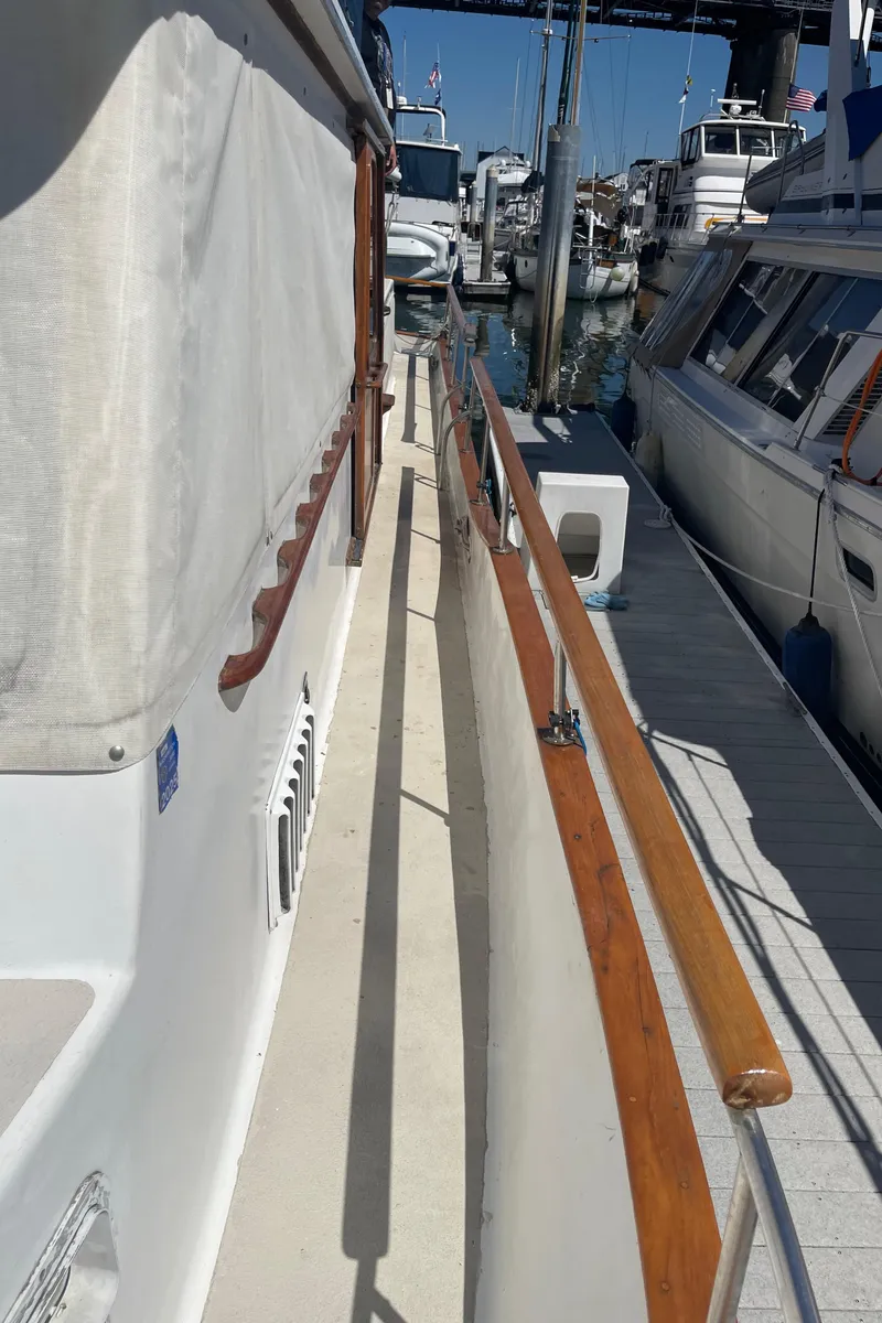 Slide: The Image of 1978 Californian Tri-Cabin Trawler docked, showcasing side deck and wooden railings. - 16