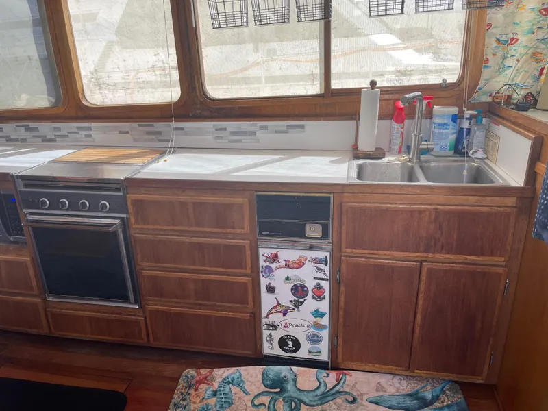 Slide: The Image of 1978 Californian Tri-Cabin Trawler kitchen with wooden cabinets, stove, and decorated fridge. - 33