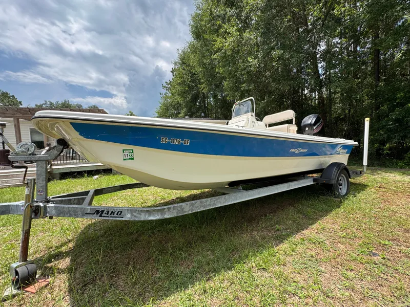 Slide: The Image of 2017 Mako Pro Skiff 19 CC boat on trailer, parked on grass, surrounded by trees. - 1