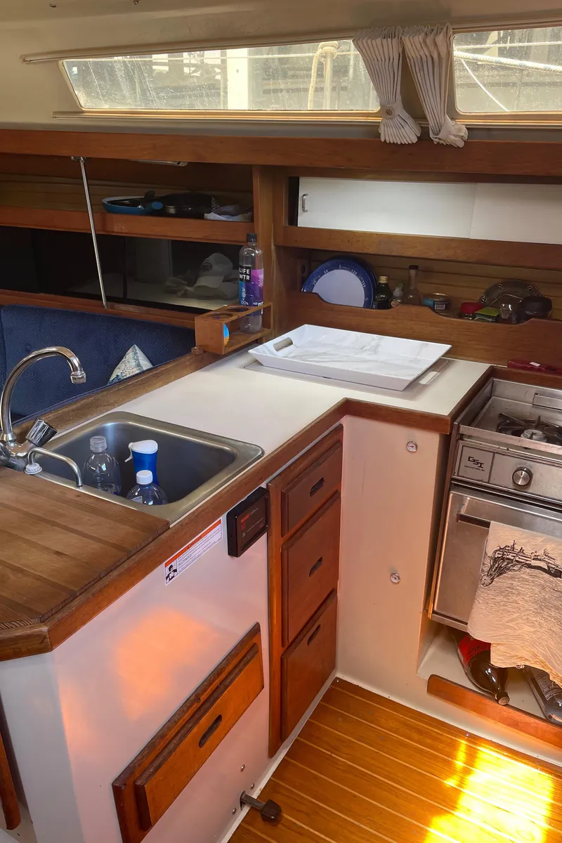 Slide: The Image of Interior of 1986 Catalina 34 sailboat galley with sink, stove, and wooden cabinetry. - 46