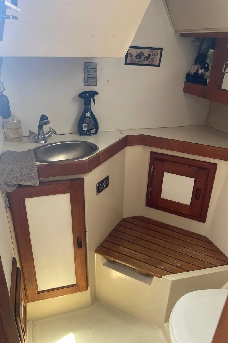 Slide: The Image of Interior of 1986 Catalina 34 sailboat bathroom with sink, wooden accents, and cleaning supplies. - 48
