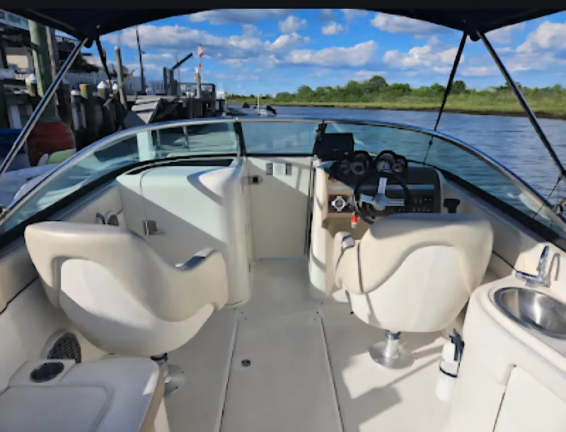 Slide: The Image of 2013 Sea Ray 260 Sundeck boat interior with steering wheel and seating, docked by the water. - 11