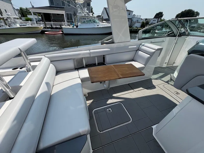 Slide: The Image of 2023 Aviara AV32 OB boat interior with sleek seating and wooden table, docked by waterfront homes. - 22