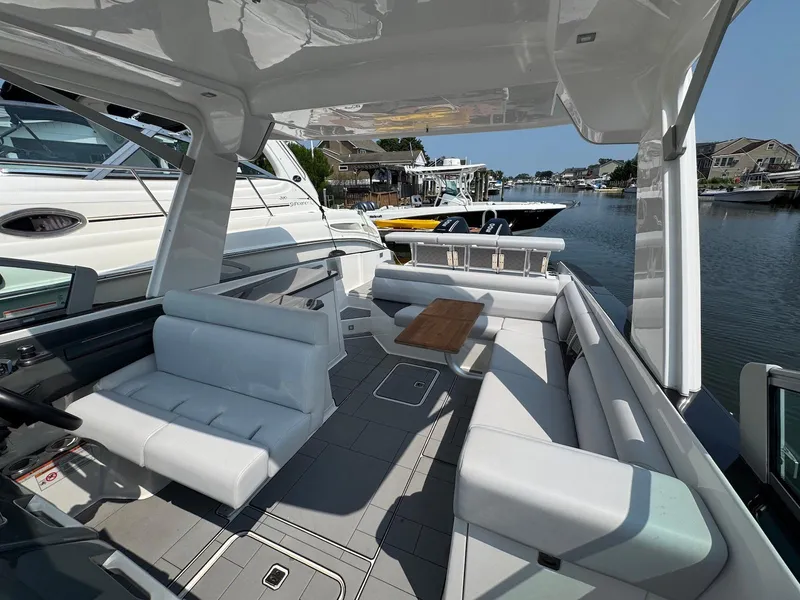 Slide: The Image of 2023 Aviara AV32 OB boat interior with sleek seating and wooden table, docked by waterfront homes. - 23