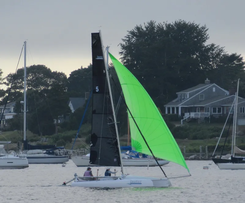 Slide: The Image of Trimaran SeaRail 19 sailing with vibrant green sail near coastal homes, 2014 model. - 2
