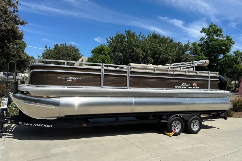 The Image of 2025 Sun Tracker Sportfish 24 XP3 pontoon boat on trailer, parked outdoors. - 0