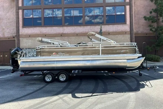The Image of 2025 Sun Tracker Sportfish 24 XP3 pontoon boat on a trailer, parked outdoors. - 0