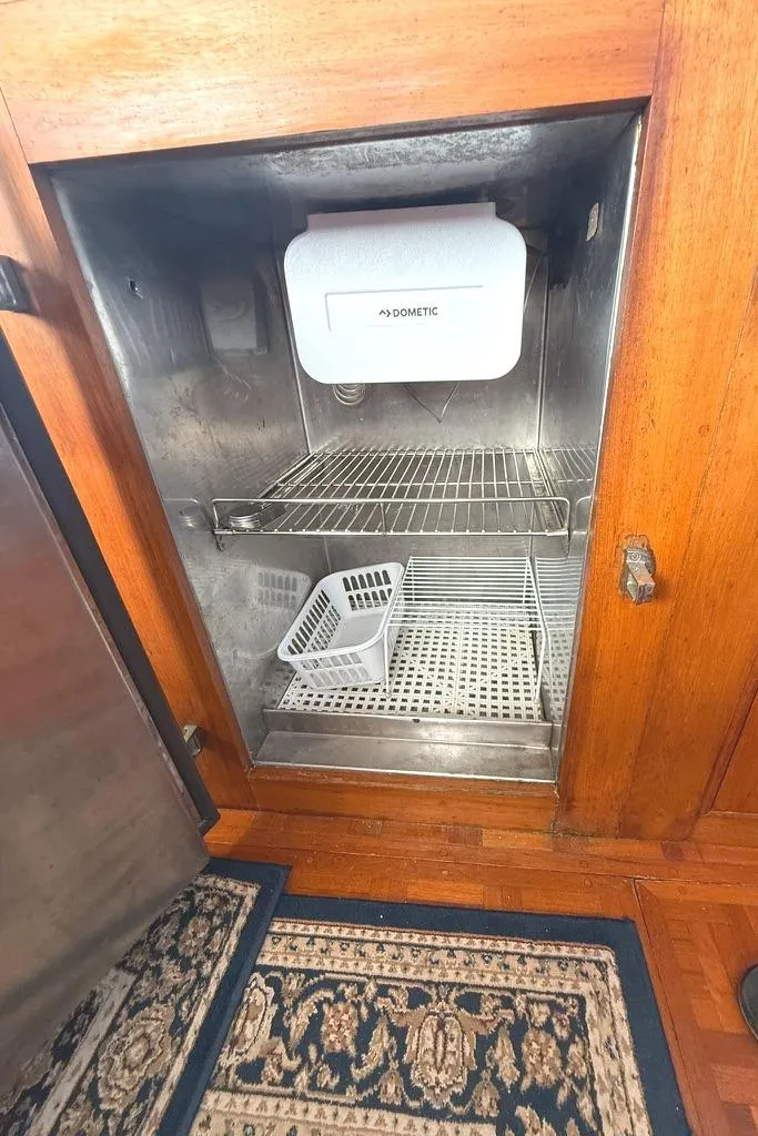 Slide: The Image of Empty refrigerator inside 1981 Grand Banks 36 Classic boat, featuring wooden cabinetry and patterned rug. - 39