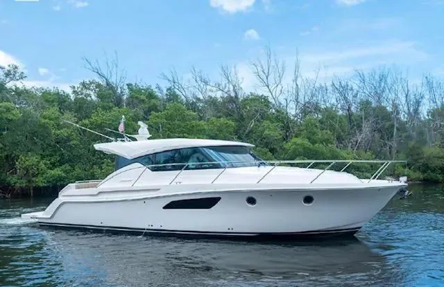 The Image of 2015 Tiara Yachts C44 Coupe cruising on a serene waterway with lush greenery. - 0