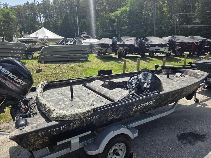Slide: The Image of 2018 Lowe 175 Stinger boat with camouflage design on a trailer, parked outdoors. - 2