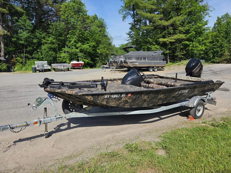 Slide: The Image of 2018 Lowe 175 Stinger boat on trailer, parked outdoors with trees in the background. - 3