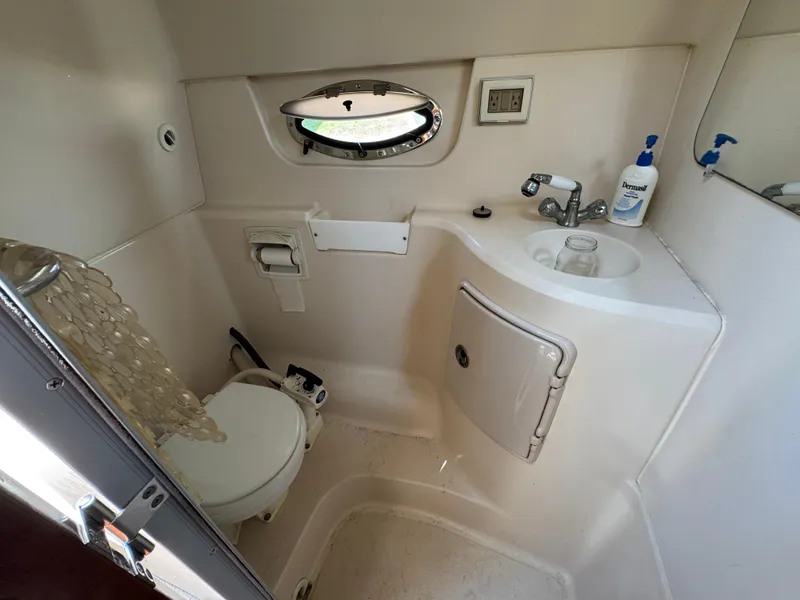 Slide: The Image of Compact bathroom in 2006 Regal 2565 Window Express boat, featuring toilet, sink, and porthole. - 27