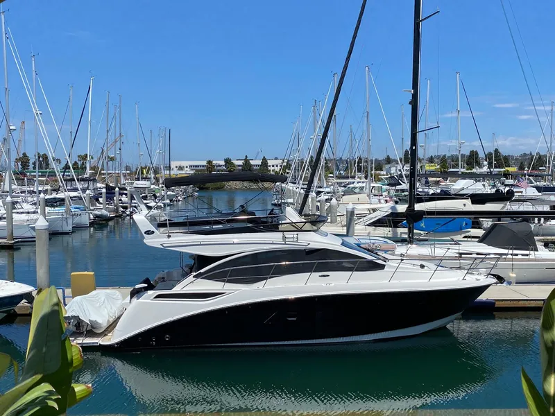 The Image of 2018 Sea Ray 400 Fly yacht docked in a marina, surrounded by sailboats. - 0