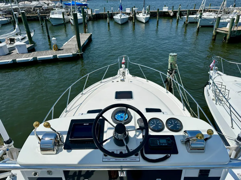 Slide: The Image of 2004 Tiara Yachts 3200 Open helm view at marina, showcasing controls and docked boats. - 9