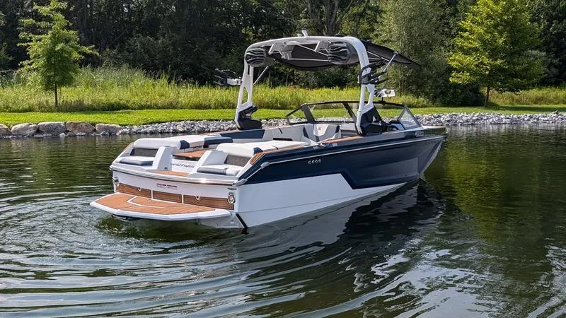 Slide: The Image of 2025 Nautique Super Air Nautique GS22 boat on a calm lake, surrounded by greenery. - 4