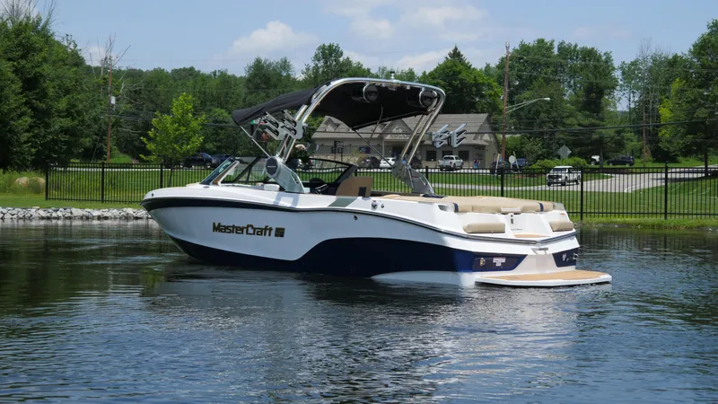Slide: The Image of 2025 MasterCraft XT23 boat on calm water, surrounded by greenery and a clear sky. - 4