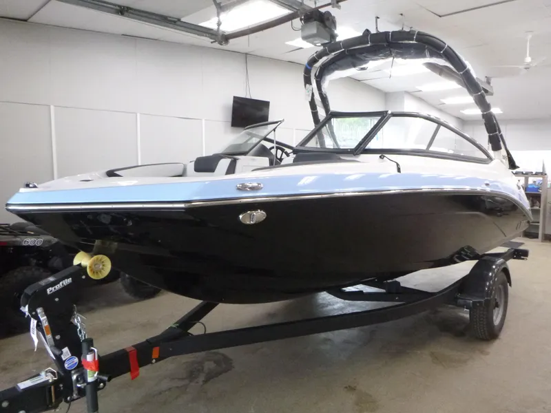 Slide: The Image of 2025 Yamaha Boats 195S in showroom, sleek design, black and white exterior, on trailer. - 2