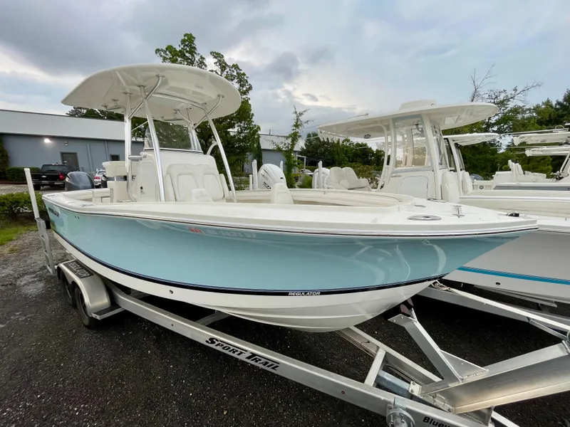 Slide: The Image of 2019 Regulator 23 boat on trailer, light blue hull, overcast sky background. - 2