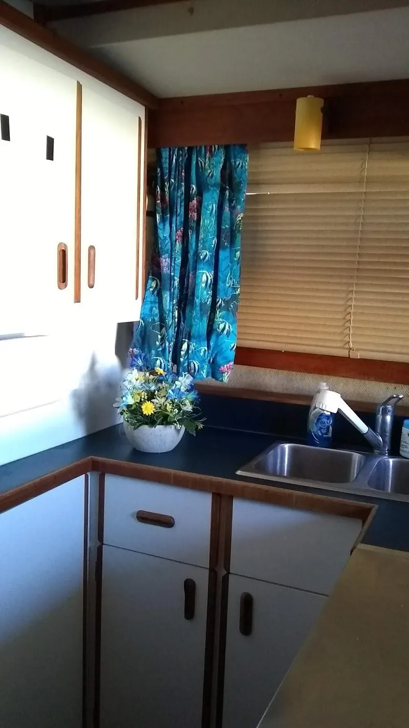 Slide: The Image of 1986 Carver 36 Mariner kitchen with blue curtains, cabinets, and a floral arrangement. - 8