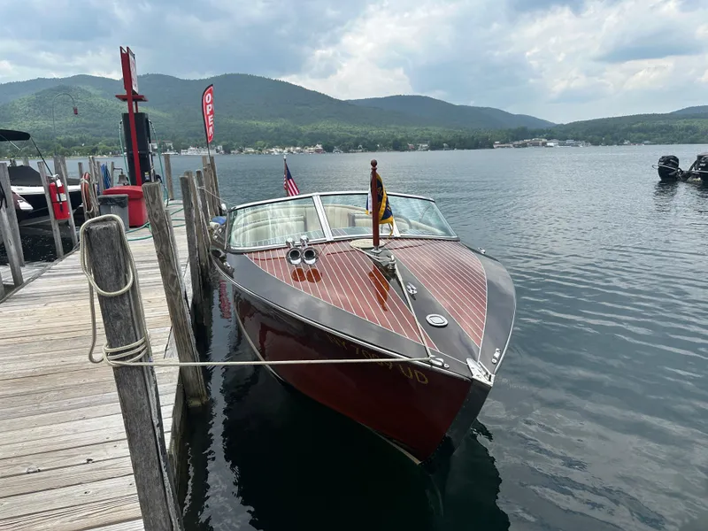 Slide: The Image of Hacker-Craft Custom Sport 1999 boat docked on a serene lake with mountains in the background. - 8