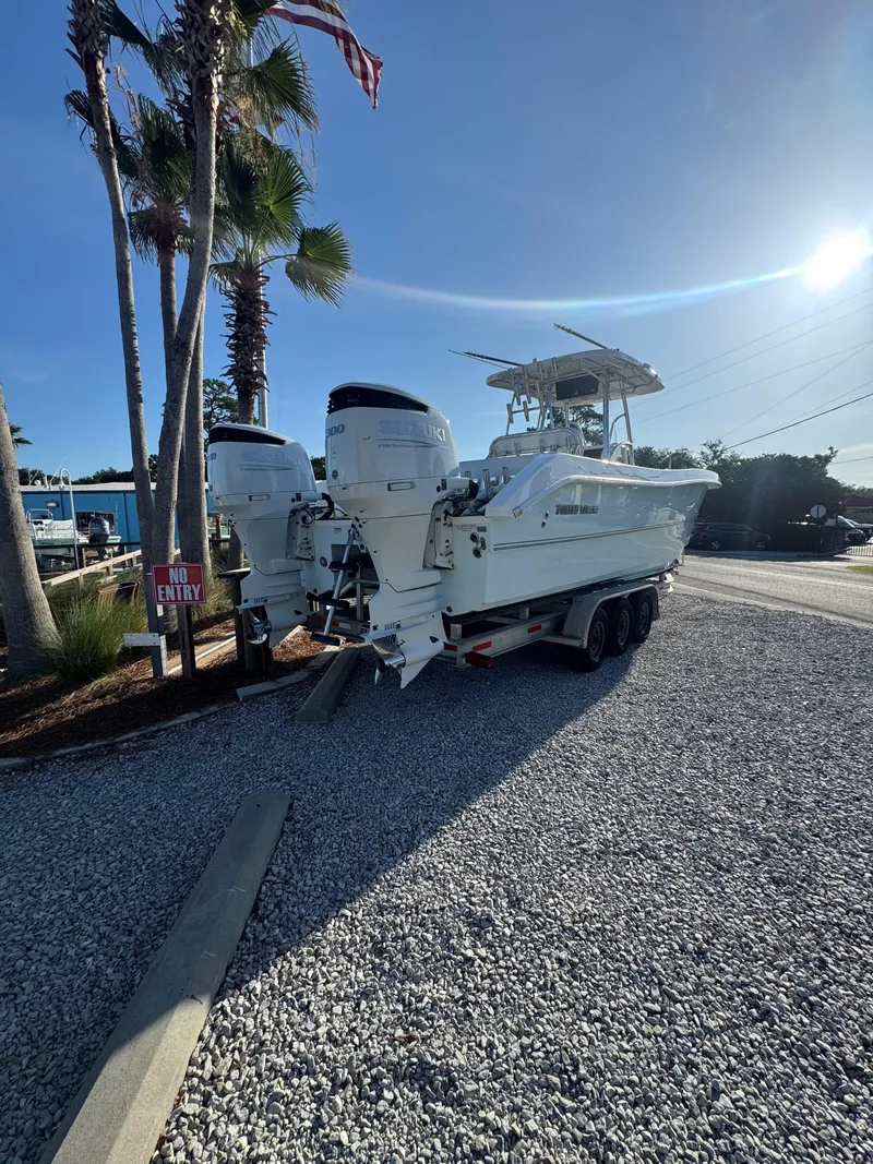 Slide: The Image of 2022 Twin Vee 310 CC GF Classic boat on trailer, parked on gravel near palm trees. - 2
