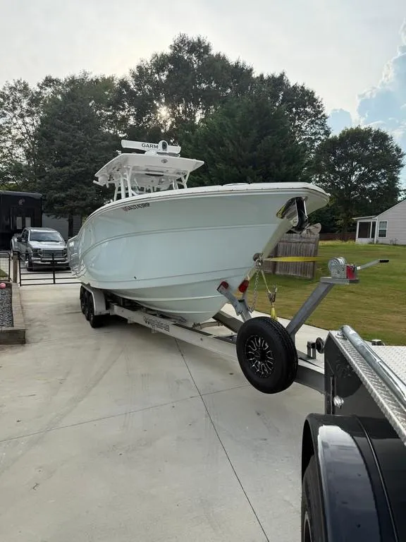 Slide: The Image of 2022 Sea Fox 328 Commander boat on trailer in driveway, surrounded by trees. - 2