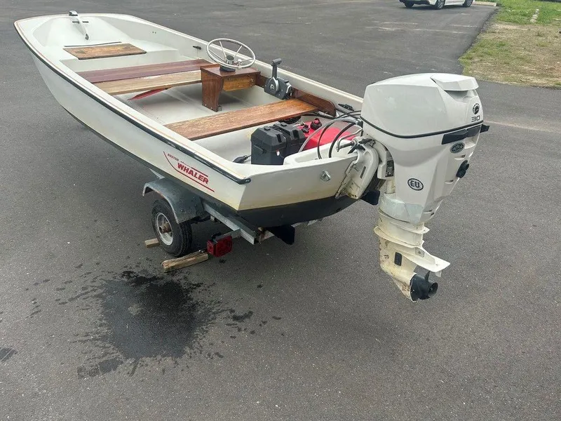 Slide: The Image of 1983 Boston Whaler Sport boat on trailer with outboard motor, parked on asphalt. - 6