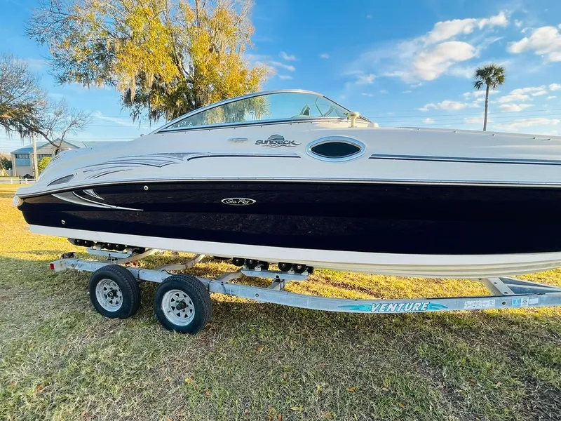 The Image of 2005 Sea Ray 240 Sundeck boat on trailer, parked on grass under blue sky. - 0