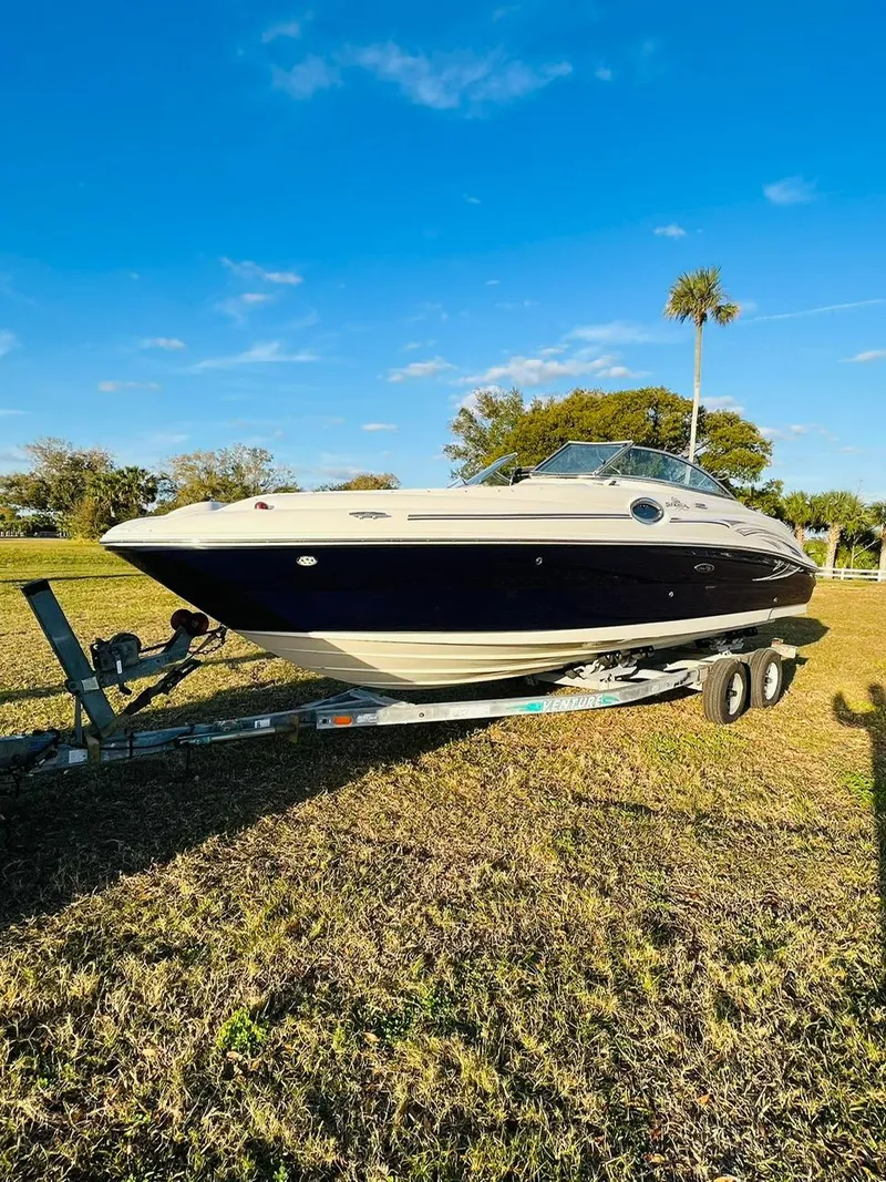 Slide: The Image of 2005 Sea Ray 240 Sundeck boat on trailer, parked on grassy field under blue sky. - 2