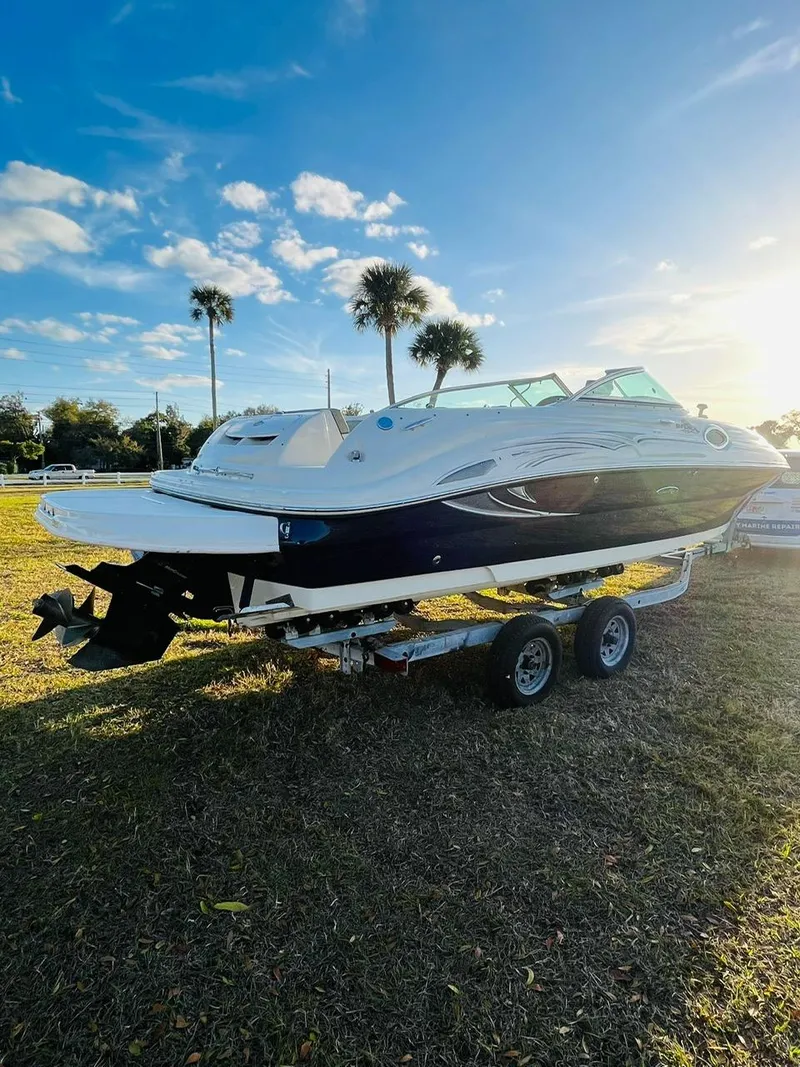 Slide: The Image of 2005 Sea Ray 240 Sundeck boat on trailer, parked on grass under a clear blue sky. - 4