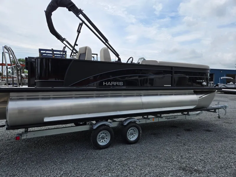 Slide: The Image of 2026 Harris Cruiser 230 pontoon boat on trailer, parked on gravel lot under cloudy sky. - 7