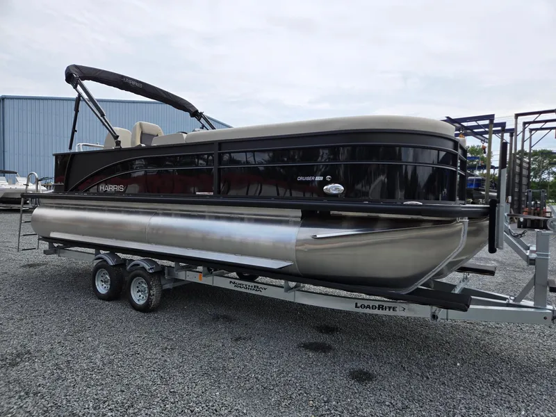Slide: The Image of 2026 Harris Cruiser 230 pontoon boat on a trailer, parked on gravel. - 8