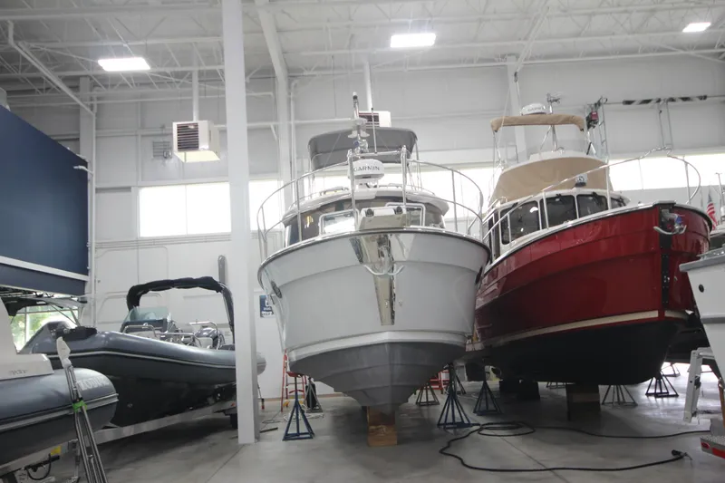 Slide: The Image of 2024 Ranger Tugs R-29 Command Bridge LE in a showroom, flanked by other boats. - 10