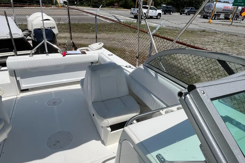 Slide: The Image of 2005 Boston Whaler 210 Ventura boat interior with seating and windshield, parked near a fence. - 28