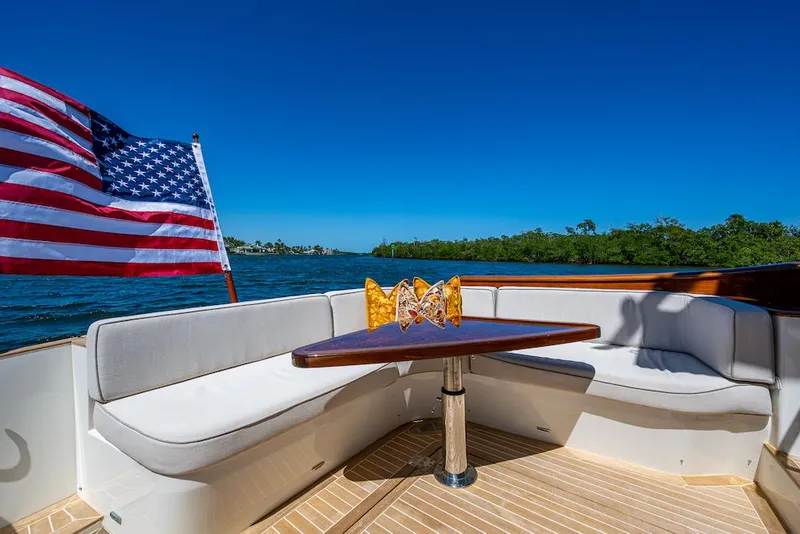 Slide: The Image of Hinckley Talaria 55 Flybridge MKII 2021 yacht deck with seating, table, and American flag. - 11