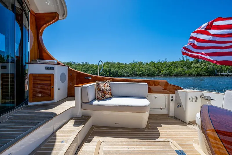 Slide: The Image of 2021 Hinckley Talaria 55 Flybridge MKII yacht deck with seating, wooden accents, and American flag. - 12