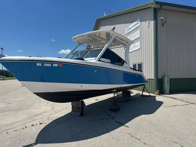 Slide: The Image of 2023 Edgewater 230CX boat interior with seating and control panel, parked outdoors. - 2