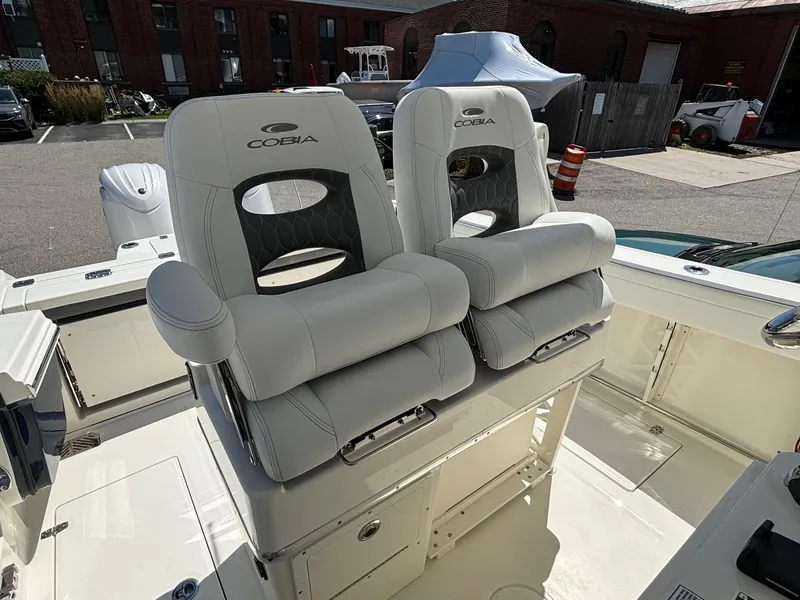 Slide: The Image of 2025 Cobia 265 Center Console boat with dual cushioned seats in a marina setting. - 20
