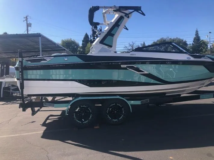 Slide: The Image of 2022 Centurion Ri 230 boat on trailer, teal and white design, parked outdoors. - 15