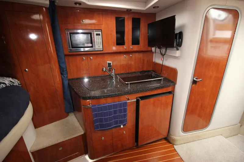 Slide: The Image of 2008 Four Winns V338 yacht interior with kitchenette, featuring wood cabinetry, microwave, and TV. - 25