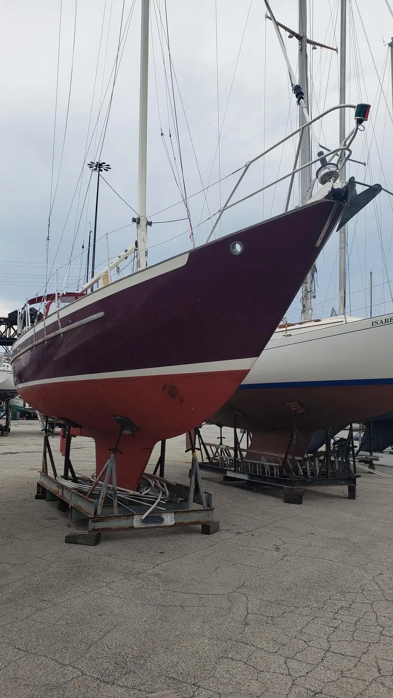 Slide: The Image of 1991 Pacific Seacraft 34 sailboat on dry dock, maroon hull, overcast sky. - 4
