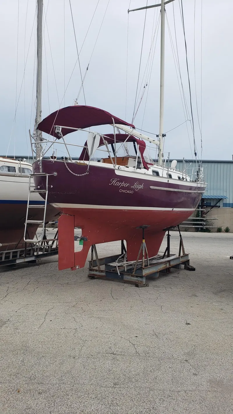 Slide: The Image of 1991 Pacific Seacraft 34 sailboat on dry dock, maroon hull, located in a marina. - 5