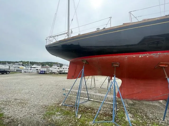 Slide: The Image of 1972 Fastnet Le Comte sailboat on stands, with red hull, in a boatyard. - 3