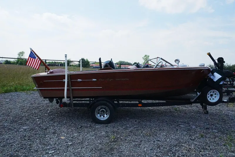 Slide: The Image of 1956 Chris-Craft Continental boat on trailer with American flag, parked outdoors. - 18